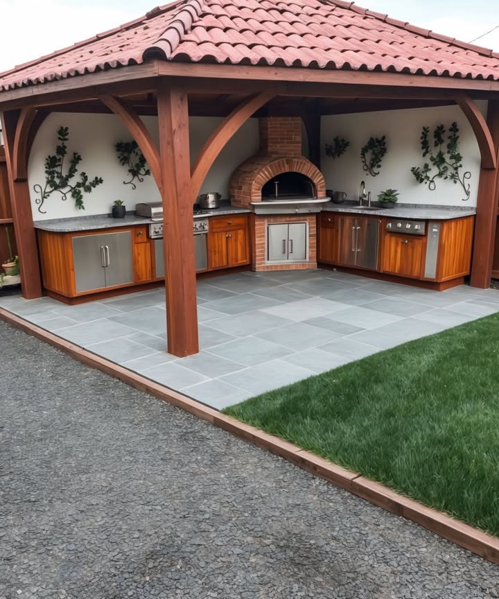 Cucine da Esterno: Il Design che Trasforma il Giardino in unOasi 

1 Struttura accogliente 
Un pergolato in legno con tetto in tegole crea ombra e protezione, senza rinunciare allatmosfera allaperto. Le travi robuste danno quel tocco rustico che fa subito casa di campagna chic.

2 Spazio funzionale 
Forno a legna e griglia diventano i protagonisti per pizza, carne e verdure alla brace. Il piano di lavoro in pietra è resistente e pratico, mentre i mobili in acciaio e legno mantengono tutto ordinato.

3 Dettagli di stile 
Pareti arricchite con decori naturali, pavimento in grandi piastrelle grigie: il mix tra rustico e moderno crea un equilibrio perfetto, facile da pulire e super elegante.

4 Paesaggio intorno 
Un prato verde fa da cornice serena, mentre il vialetto in ghiaia aggiunge texture e comodità di accesso. Insomma, non solo cucina ma un vero angolo di relax.

5 I vantaggi 

Ideale per barbecue, feste e serate in famiglia allaperto

Aumenta il valore dellimmobile chi non sogna una cucina così?

Offre unesperienza culinaria diversa e conviviale, dove i sapori si uniscono al contatto con la natura

Questa cucina da esterno dimostra come un design ben studiato possa trasformare il giardino in uno spazio funzionale e suggestivo. Un piccolo rifugio moderno dove cucinare diventa un piacere e mangiare una festa! 壟